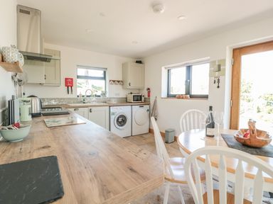 A kitchen with wooden countertop white cabinets a round dining table with chairs a wine bottle and glasses at Black Cat Bach in Gilwern