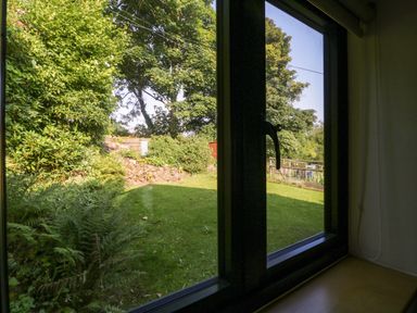 A view of a garden with green grass trees and bushes seen through a closed window at Black Cat Bach in Gilwern