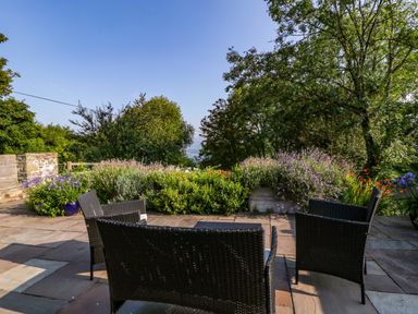 An outdoor patio with black wicker chairs and a table surrounded by plants and trees at Black Cat Bach in Gilwern