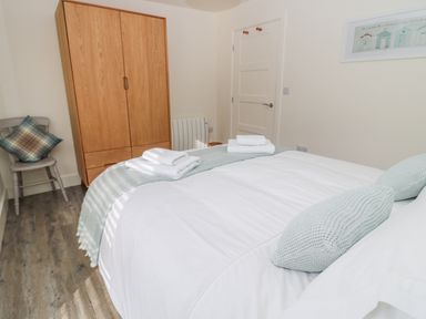 A bedroom with a bed with pillows and towels a wooden wardrobe a chair with a cushion and a door at Lambs Lodge in Bamburgh
