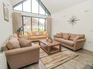 A living room with two brown sofas a yellow sofa a wooden coffee table and a telescope near a large window at Lambs Lodge in Bamburgh