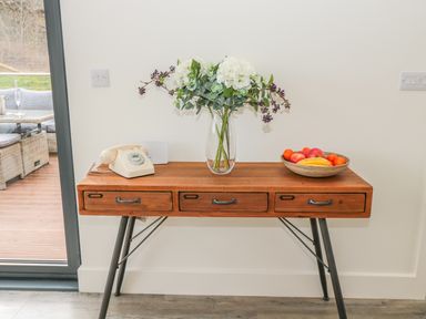 A wooden table with drawers holding a rotary phone a vase with flowers and a bowl of fruit at Lambs Lodge in Bamburgh