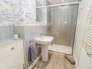 A bathroom with a sink a glass door shower a towel ring with a gray towel and patterned wallpaper at Lambs Lodge in Bamburgh