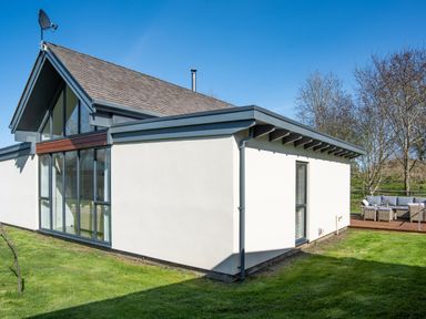 A modern house with large glass windows and patio furniture on a deck at Lambs Lodge in Bamburgh