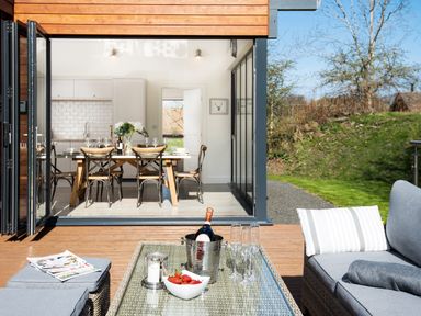 An outdoor seating area with a table holding a wine bottle in a cooler glasses and a bowl of strawberries with a dining area visible through open glass doors at Lambs Lodge in Bamburgh