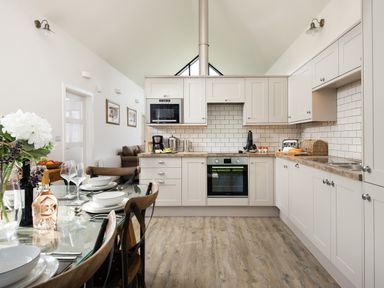A kitchen with white cabinets a dining table set with plates and glasses and a seating area visible at Lambs Lodge in Bamburgh