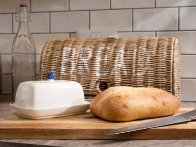 A kitchen countertop with a loaf of bread, a bread knife, a butter dish, and a wicker bread box at Lambs Lodge in Bamburgh