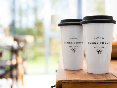 Two white travel mugs with black lids on a wooden table at Lambs Lodge in Bamburgh