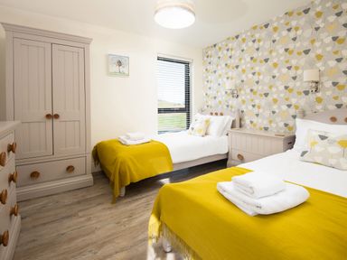 A bedroom with two single beds yellow blankets and white towels a wardrobe a chest of drawers and a window at Lambs Lodge in Bamburgh