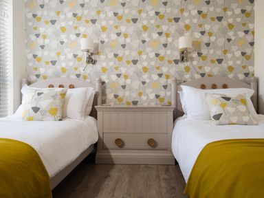 A bedroom with two single beds a chest of drawers wall lamps and patterned wallpaper at Lambs Lodge in Bamburgh