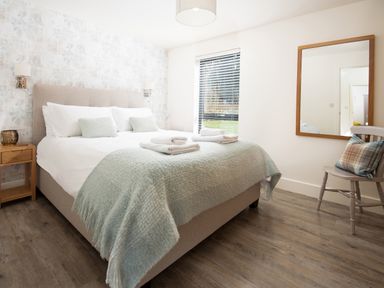 A bedroom with a bed table chair mirror and window at Lambs Lodge in Bamburgh