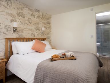 A bedroom with a wooden bed white and gray bedding a bedside table and a tray with breakfast items at Lambs Lodge in Bamburgh