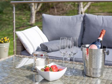 An outdoor seating area with a glass table holding champagne glasses a bottle in an ice bucket strawberries and a candle at Lambs Lodge in Bamburgh