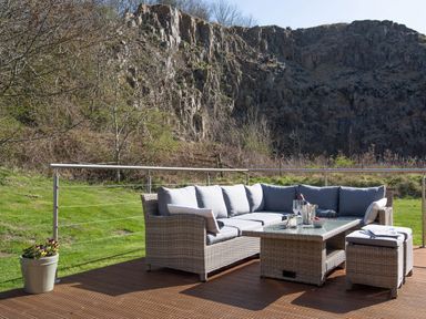 An outdoor seating area with a wicker sofa set on a wooden deck in front of a rocky hillside