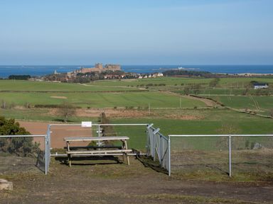 A picnic bench overlooking green fields with a castle and the sea in the background at Lambs Lodge in Bamburgh
