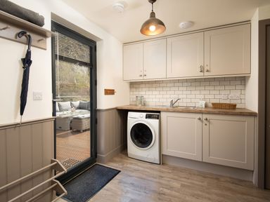 A utility room with washing machine sink cabinets and umbrella near glass door at Lambs Lodge in Bamburgh