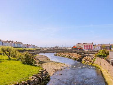 A river with a pedestrian bridge crossing it and houses on both sides by Bari in Aberaeron