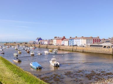 A harbor with boats anchored in water and colorful buildings along the waterfront at Bari Aberaeron