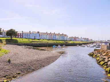 A river with boats docked along the shore and a row of colorful houses on a grassy bank at Bari in Aberaeron