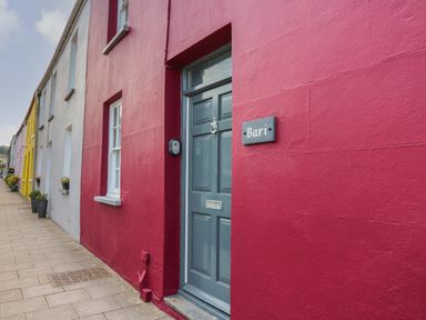 A row of colorful houses along a sidewalk with a blue door and a sign that says Bari in Aberaeron