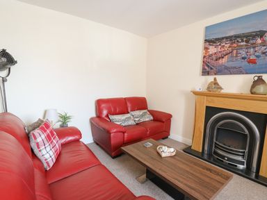 A living room with red leather sofas a wooden coffee table and a fireplace with a painting above at Bari Aberaeron