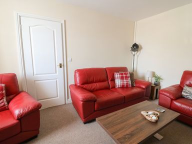 A living room with red leather sofas a wooden coffee table and a white door at Bari in Aberaeron