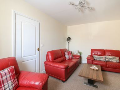 A living room with red leather sofas a wooden coffee table and a white door at Bari in Aberaeron