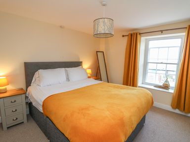 A bedroom with a double bed covered with an orange blanket two bedside tables with lamps a window with orange curtains and a full-length mirror at Bari in Aberaeron