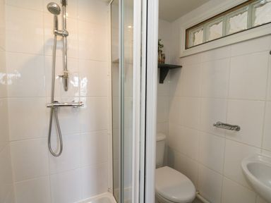 A bathroom with a shower, toilet, small sink, and a high window at Bari in Aberaeron