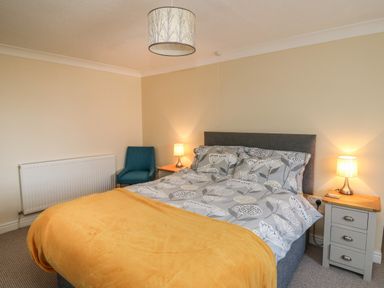 A bedroom with a double bed with floral bedding and a yellow blanket bedside tables with lamps and a blue armchair at Bari in Aberaeron