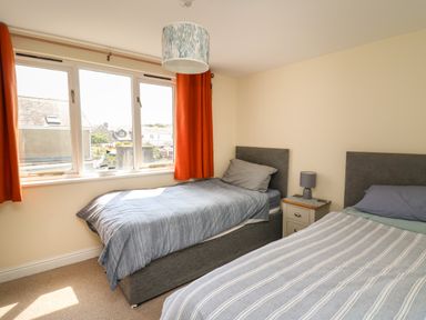 A bedroom with two single beds a nightstand and a window with orange curtains at Bari in Aberaeron