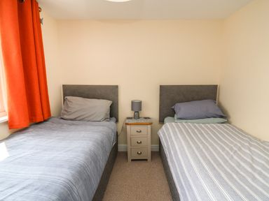 A bedroom with two single beds separated by a small bedside table with a lamp and an orange curtain at Bari in Aberaeron
