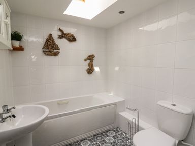 A bathroom with a bathtub pedestal sink toilet wall decorations and patterned floor tiles at Bari Aberaeron
