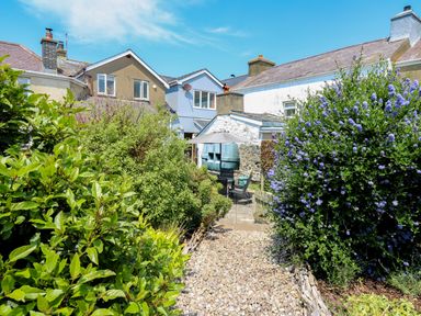 A backyard garden with a gravel pathway leading to a patio with chairs and an umbrella at Bari in Aberaeron