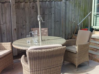An outdoor patio area with a round glass-top table and four wicker chairs with cushions at Meadow View Cottage in Lympstone
