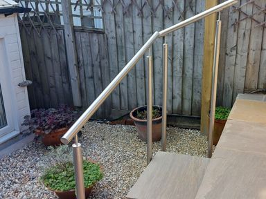 A stainless steel handrail on stone steps leading to a gravel area with potted plants and a wooden fence at Meadow View Cottage in Lympstone