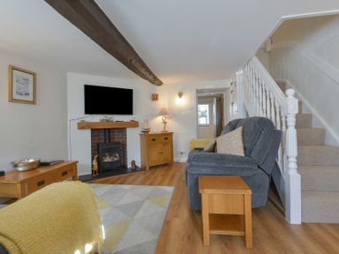 A living room with a gray sofa wooden tables a fireplace wall-mounted TV and a staircase at Meadow View Cottage in Lympstone