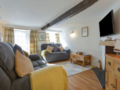 A living room with gray sofas and yellow cushions a wooden coffee table mounted TV and wooden furniture at Meadow View Cottage in Lympstone
