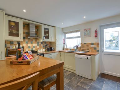A kitchen with wooden countertops a dining table and chairs and a dishwasher at Meadow View Cottage in Lympstone