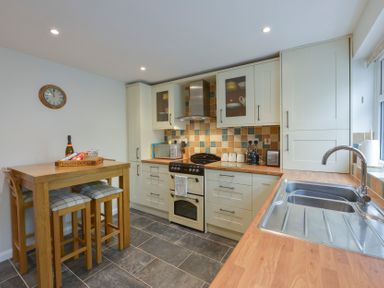 A kitchen with a wooden table and stools and a stove with tiled backsplash at Meadow View Cottage in Lympstone