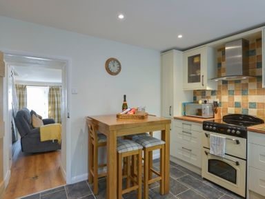 A kitchen with a wooden table and stools a stove microwave and tiled backsplash at Meadow View Cottage in Lympstone