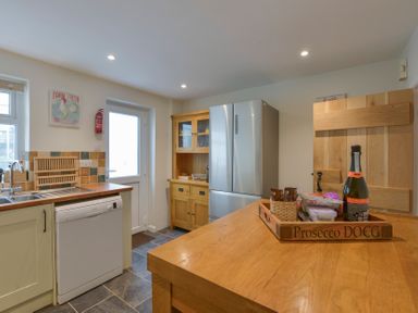 A kitchen with a wooden island, refrigerator, dishwasher, sink, wooden cabinet, and a door at Meadow View Cottage in Lympstone