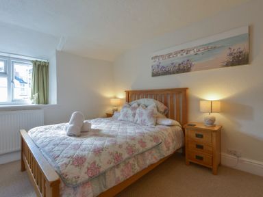 A bedroom with a wooden bed and floral bedding beside bedside tables with lamps at Meadow View Cottage in Lympstone