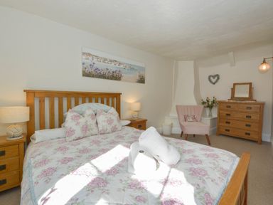 A bedroom with a wooden bed with floral bedding a wooden dresser a pink chair and two bedside tables with lamps at Meadow View Cottage in Lympstone