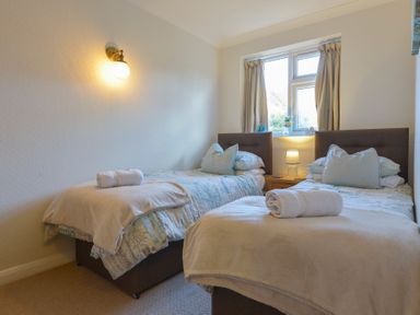 A bedroom with two single beds with pillows and towels near a window with curtains at Meadow View Cottage in Lympstone