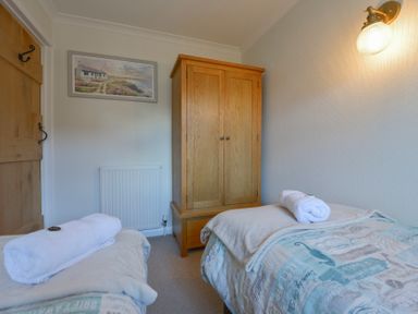 A small bedroom with two single beds a wooden wardrobe a wall light and a framed picture at Meadow View Cottage in Lympstone
