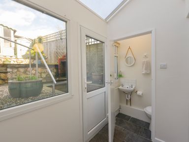 A small bathroom with a sink mirror towel and toilet next to a door and window showing an outdoor garden area at Meadow View Cottage in Lympstone