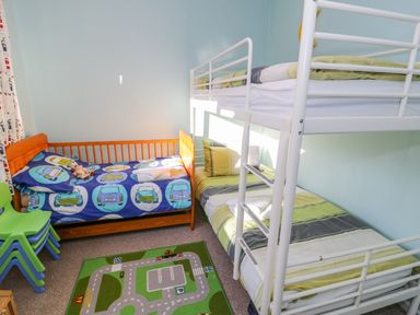 A children's bedroom with bunk beds a single bed with car themed bedding stacked green chairs and a play mat with a road design at Clyd Fan in Harlech