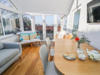 A dining area with a wooden table and chairs next to a sitting area with sofas and large windows at Clyd Fan in Harlech