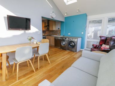 A kitchen and dining area with wooden table and chairs washing machines and armchairs at Clyd Fan in Harlech